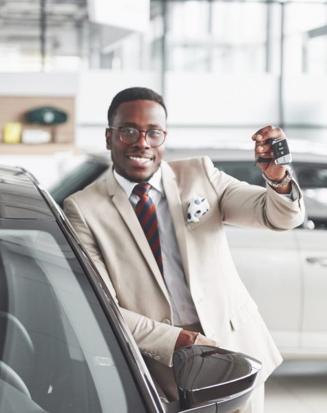 Handsome black man in dealership is hugging his new car and smiling.